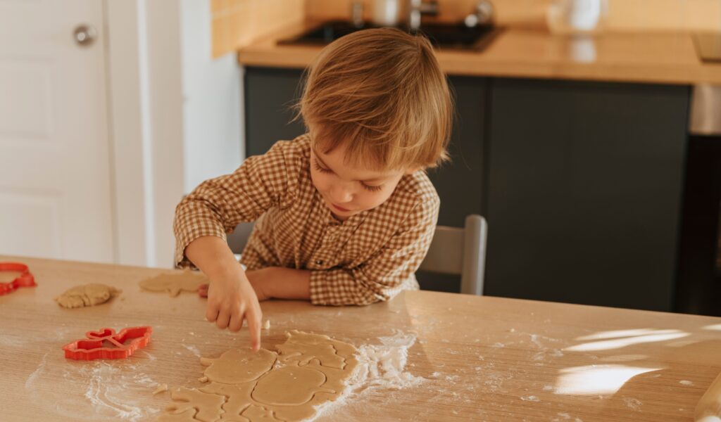 Enfant qui fait de la pâtisserie découpant de la pâte et jouant avec les ingrédients sur un plan de travail fariné.