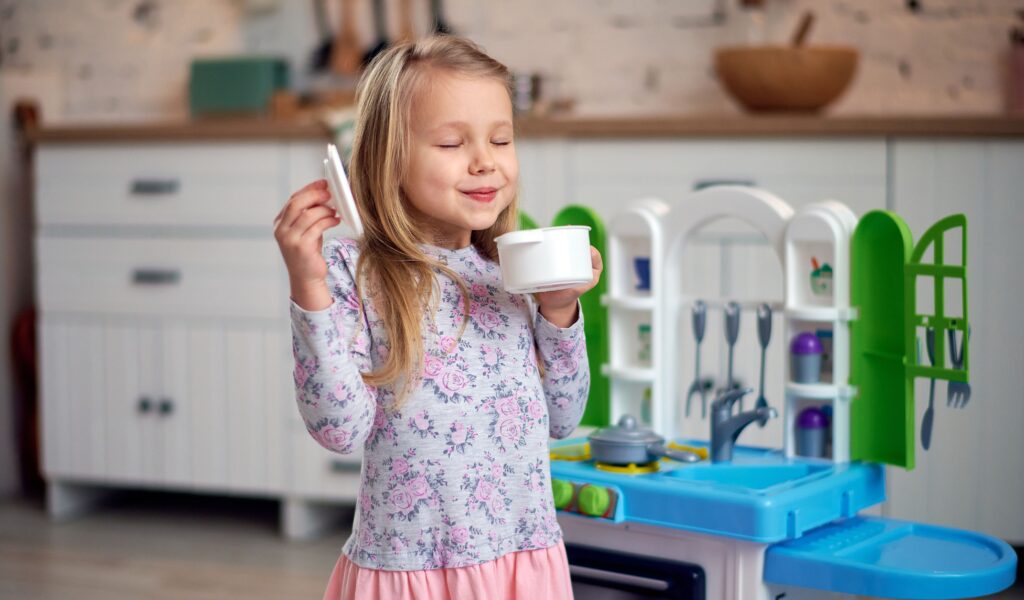 Enfant préparant une recette imaginaire dans une cuisine miniature lors d'une activité de jeu symbolique.